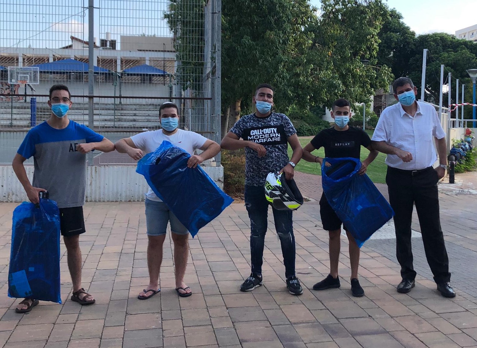 תמונה של ראש העיר ונציגי צעירים לפני גיוס עומדים בגינה ציבורית עם שי מהעירייה - תיק גב