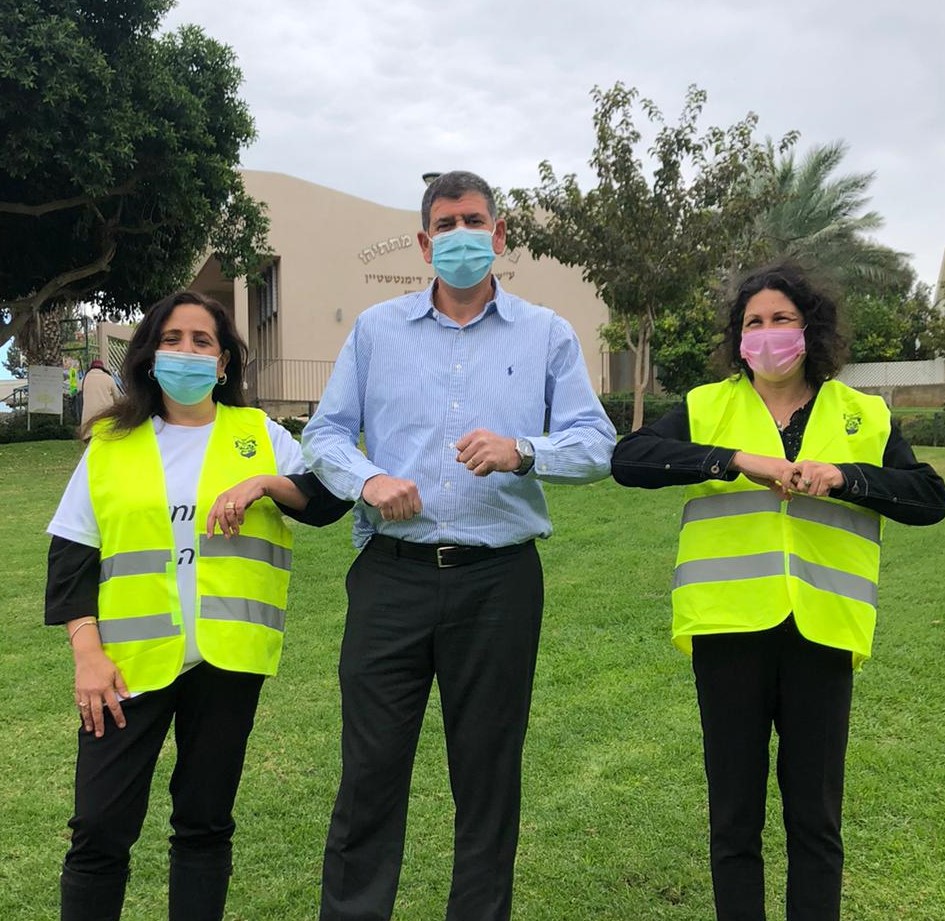 ראש העיר יוסי ברודני עם שתי מתנדבות עוטות וסטים זוהרים ומסכות